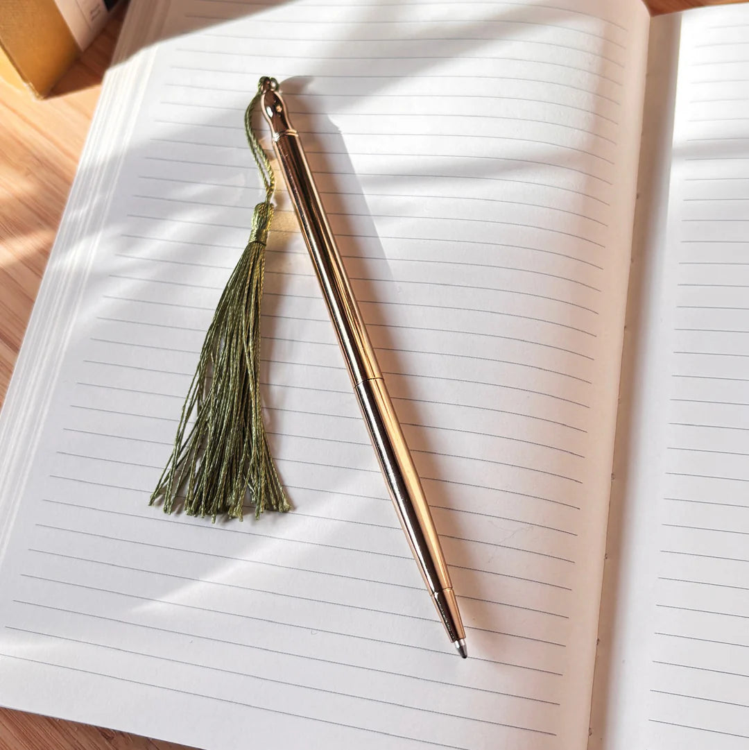 Rose gold pen with a green tassel on an open notebook