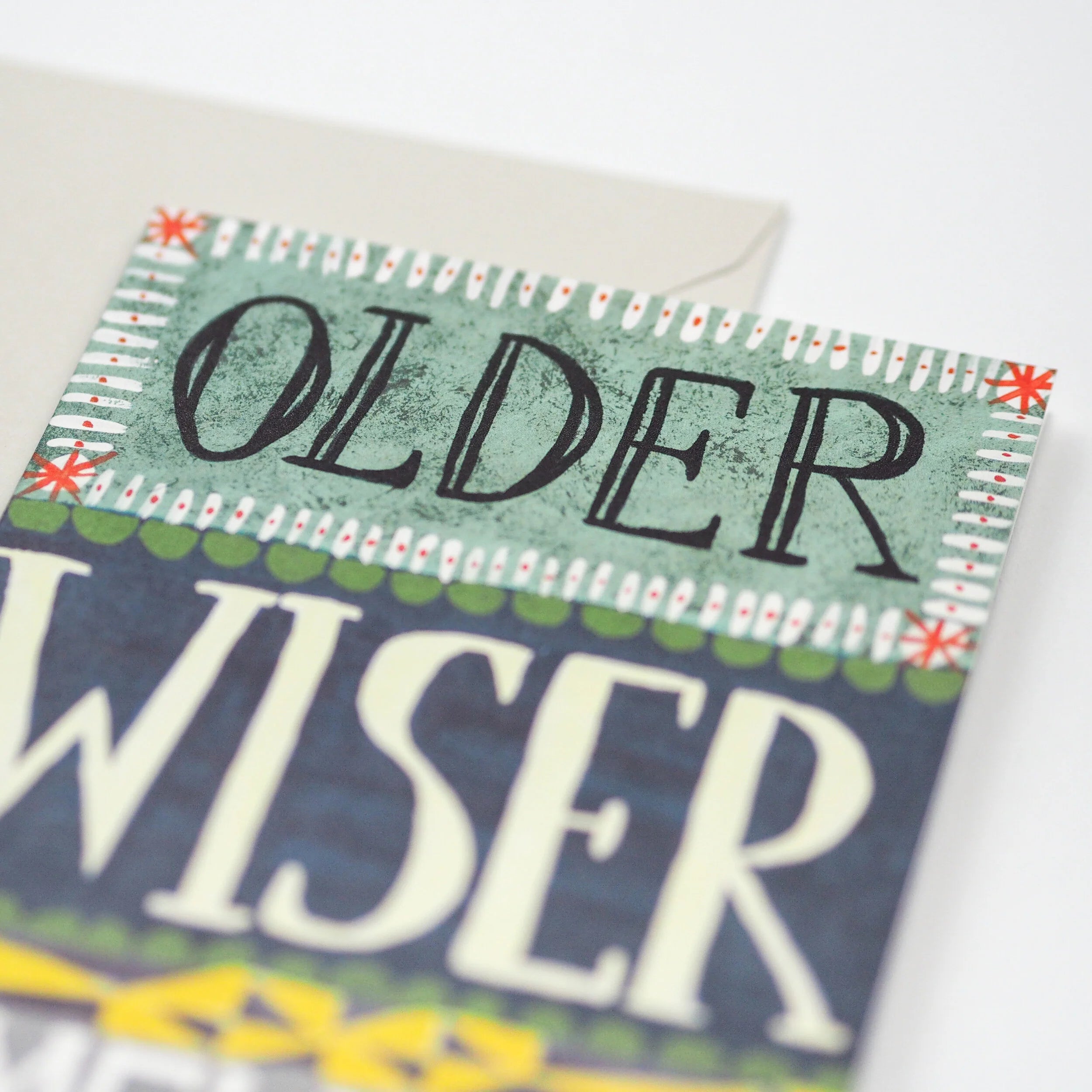 Birthday card with "Older Wiser" in stylized lettering on a teal background with decorative borders.