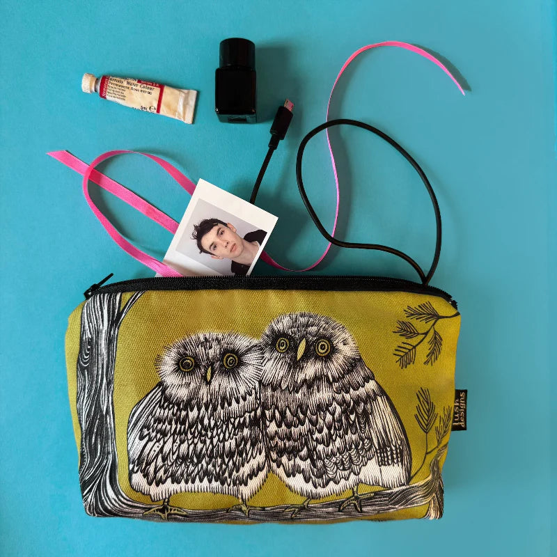 Yellow pouch with owl design containing a photo, tube, and other items on a blue background