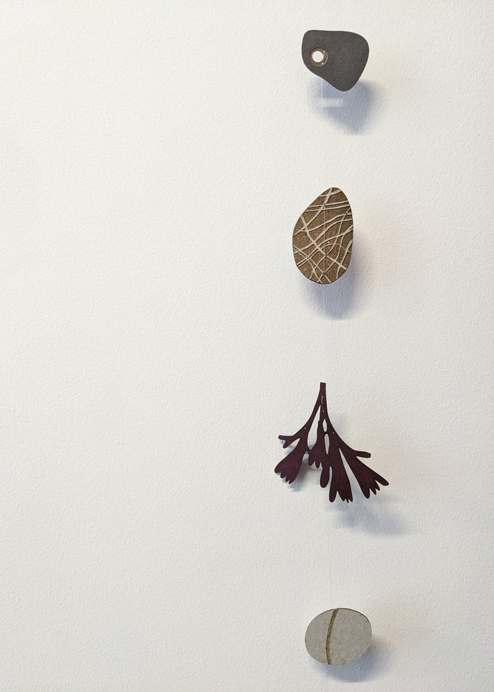 Abstract mobile with four hanging elements: a dark gray irregular shape, a light brown textured oval, a dark burgundy