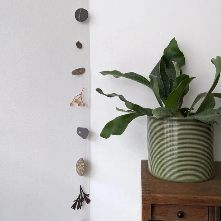 Wall hanging featuring a vertical arrangement of small, textured, gray and beige stone and botanical shapes.