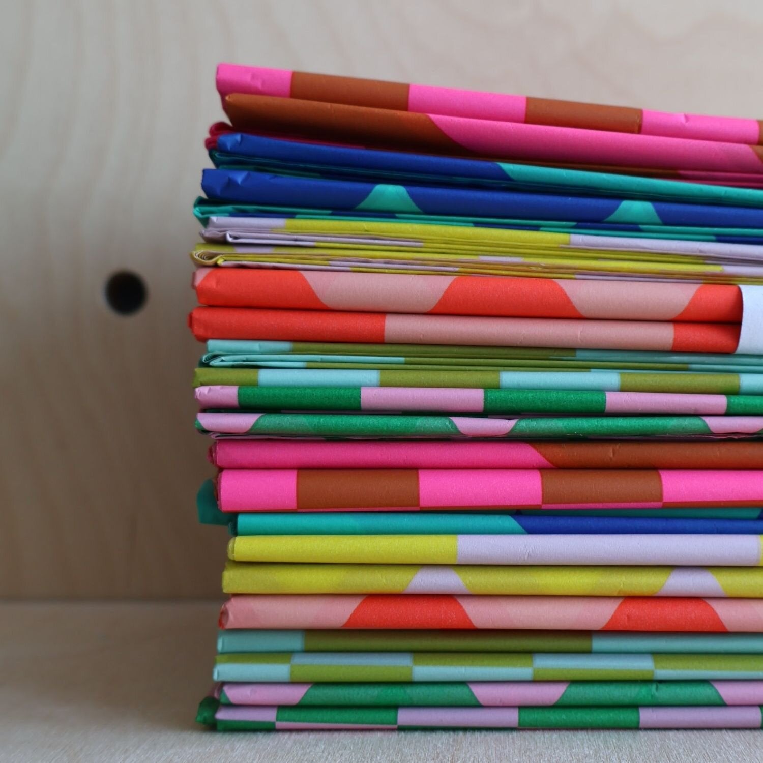 Stack of colorful patterned paper sheets. Geometric designs in various bright colors.