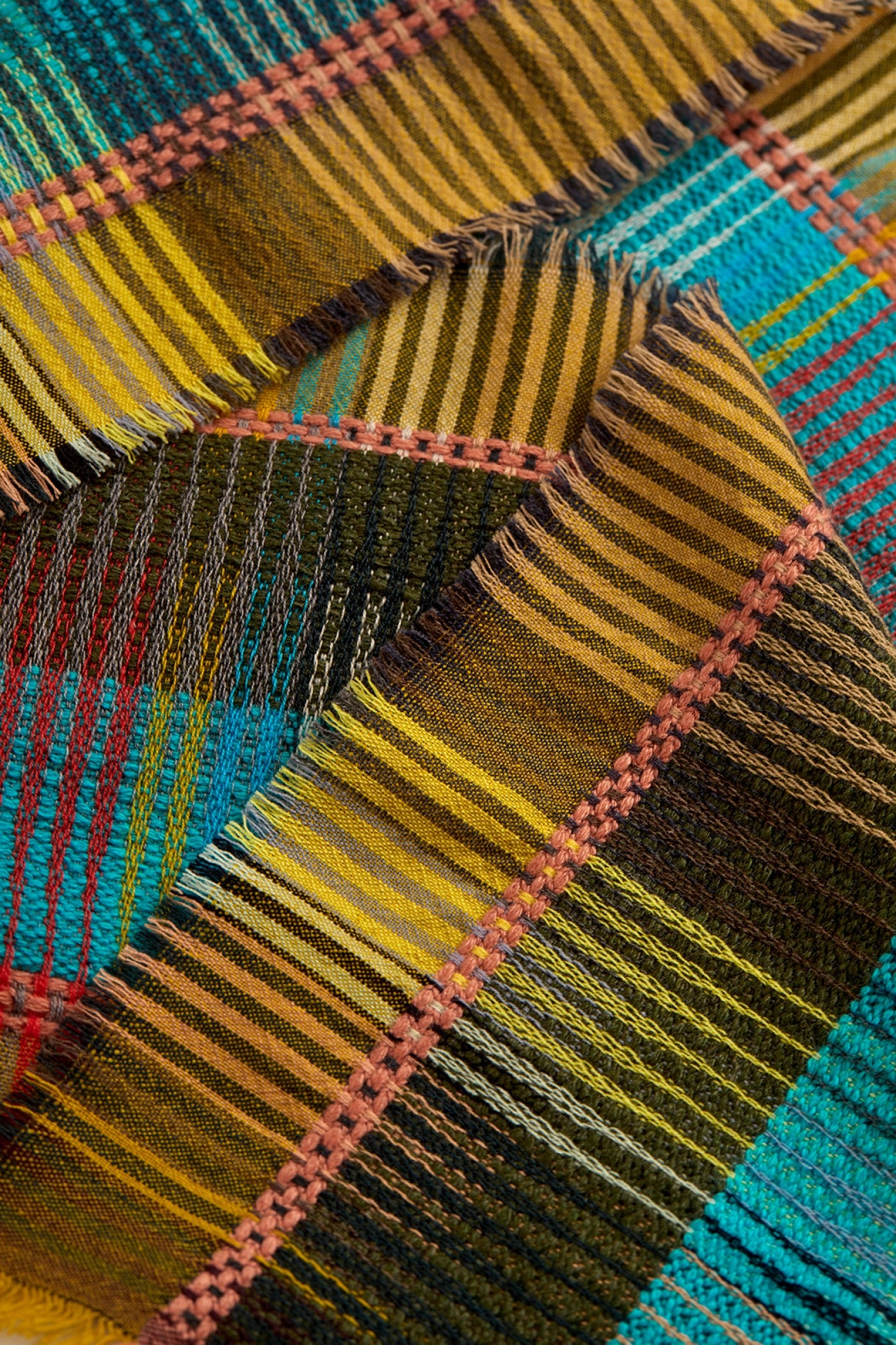 A close-up of a plaid fabric with a multicolor pattern featuring yellow, brown, teal blue, pink, and black stripes.