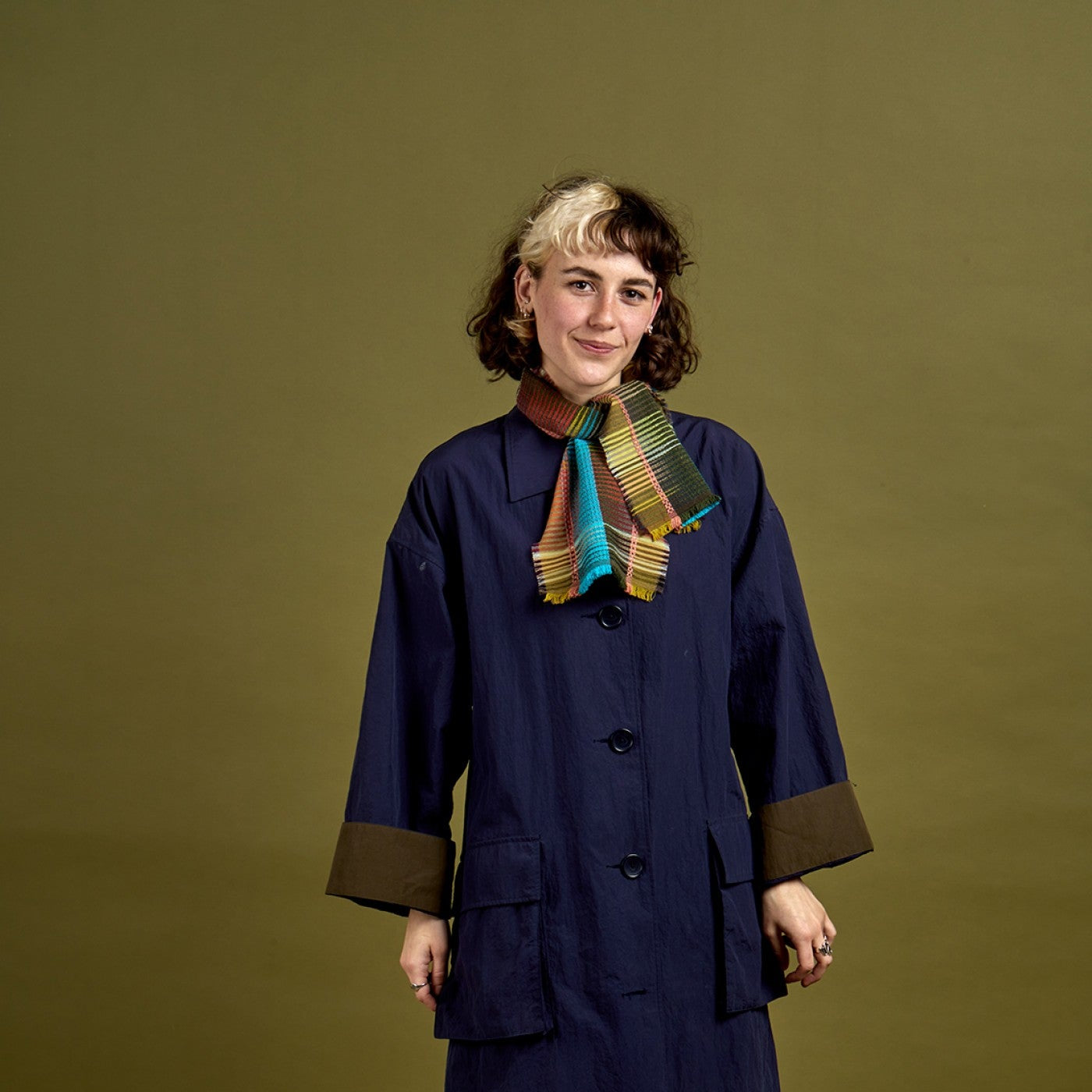 Person wearing a long dark coat with a colorful scarf against a green background