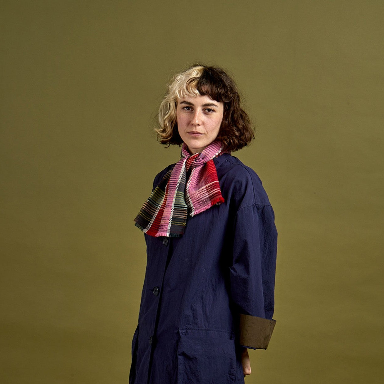 Person wearing a long dark coat and plaid scarf against a green background
