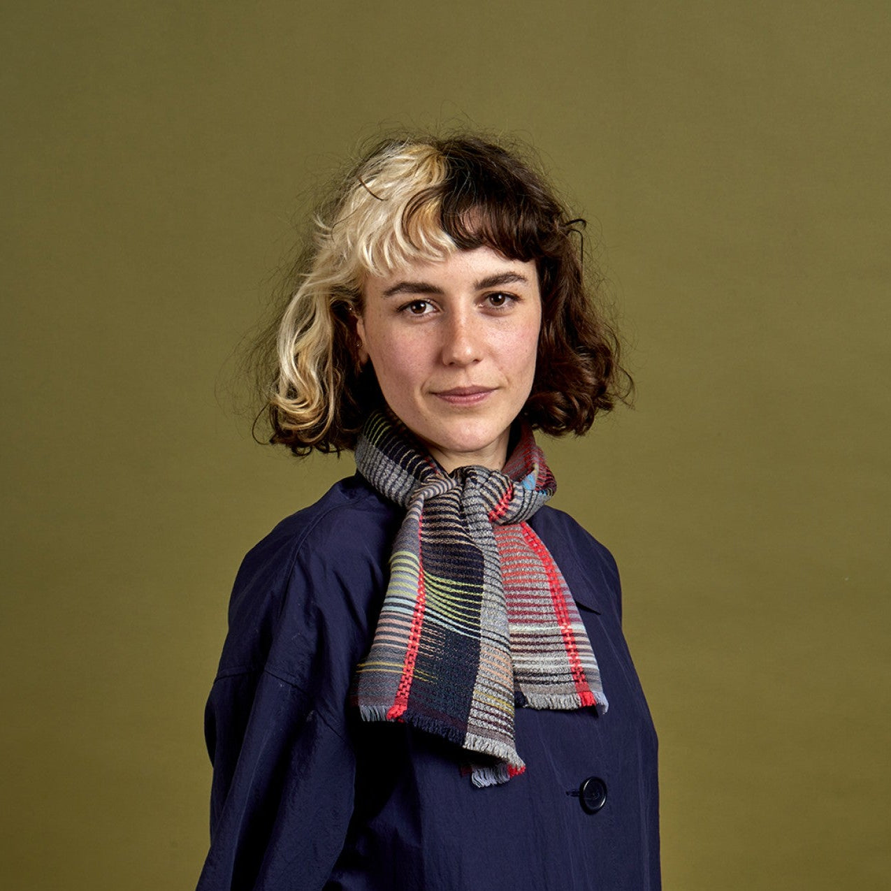 Woman wearing a navy coat and plaid scarf against a green background
