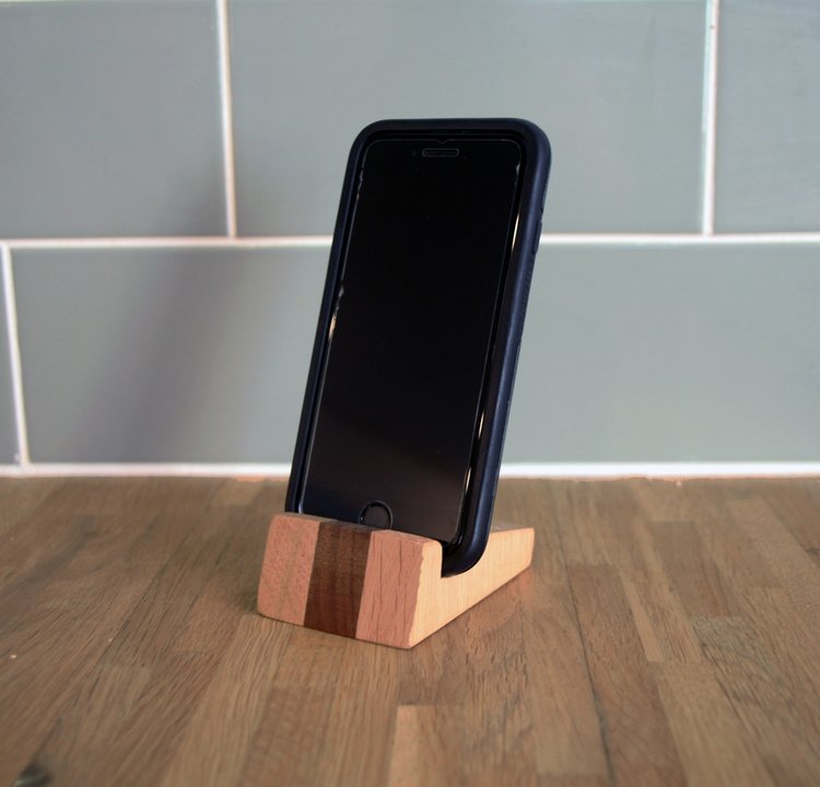 Smartphone in a wooden stand. The stand is light-colored wood with a darker wood accent.