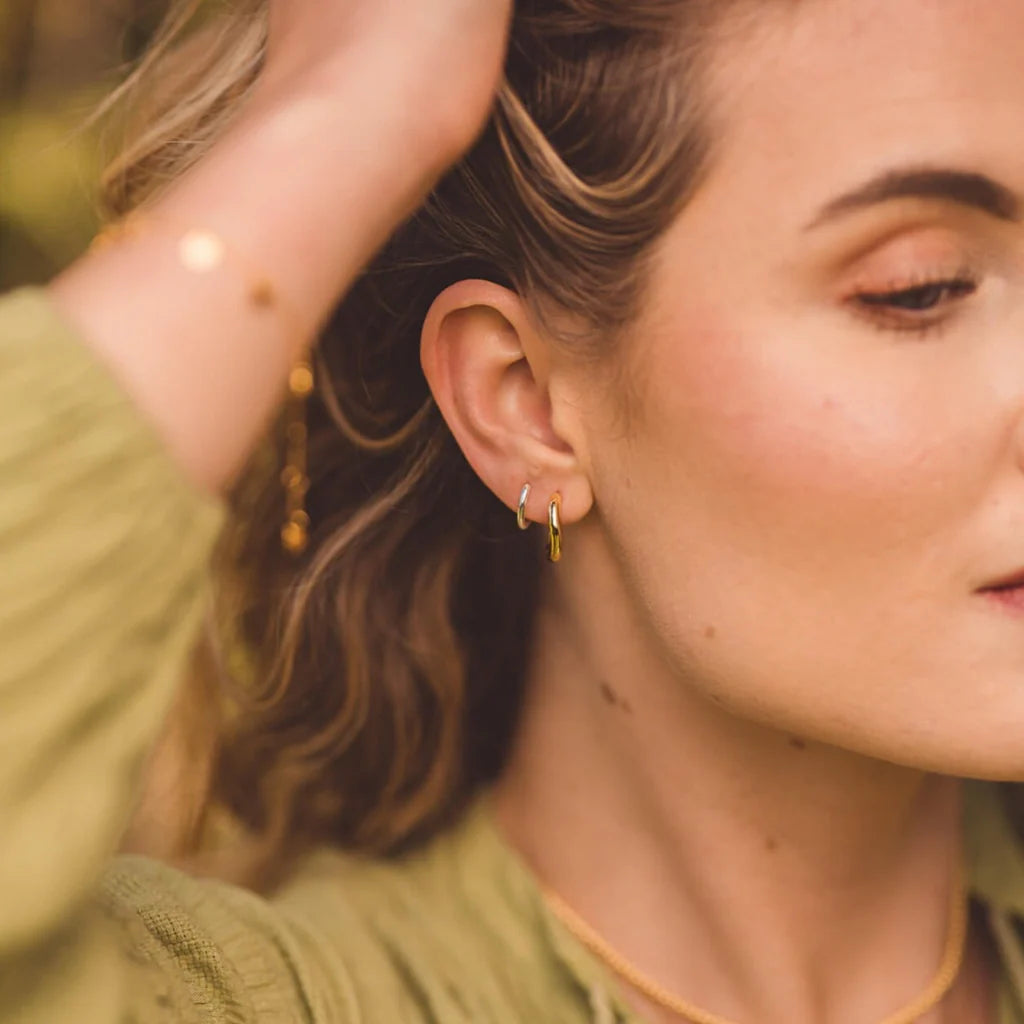 Gold and silver small hoop earrings worn in a woman's ear.