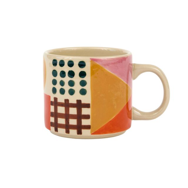 A ceramic mug with a colorful geometric pattern featuring pink, orange, yellow, and dark green shapes on a cream background, shown against a plain white background.
