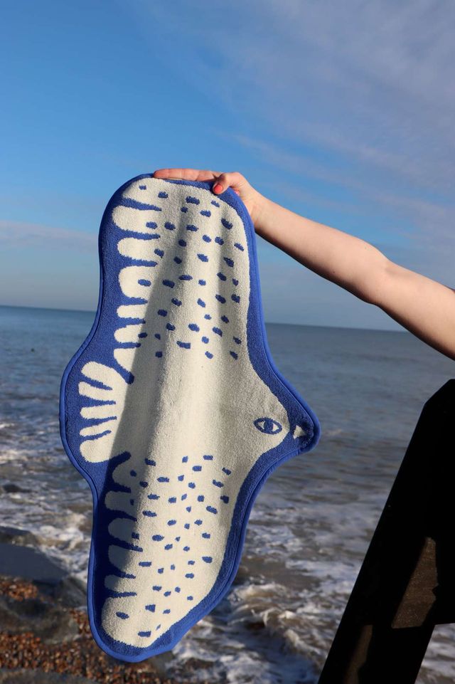 Person holding a shark-shaped towel with ocean and sky in the background