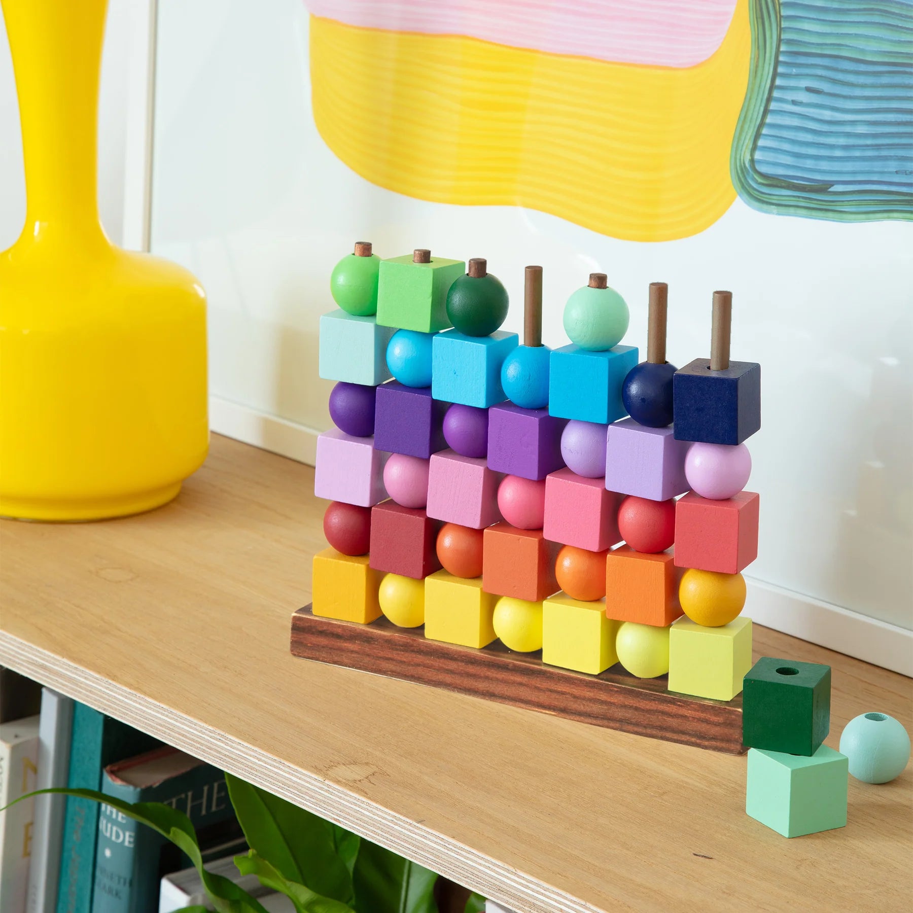 Colorful geometric toy on a wooden surface with a yellow vase and colorful umbrella in the background.