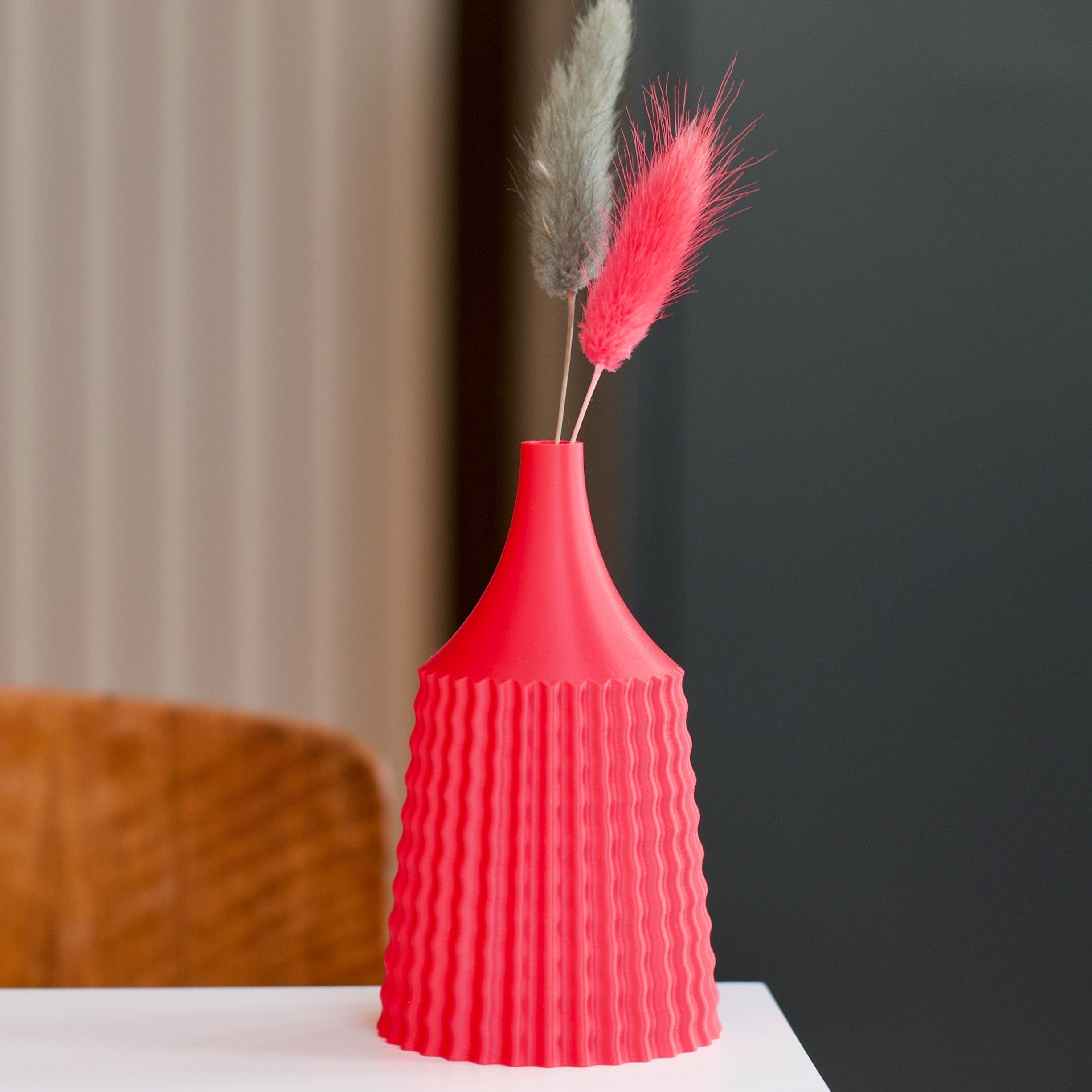 Bright red, 3D-printed vase with a textured, ribbed surface, holding gray and pink dried flowers.