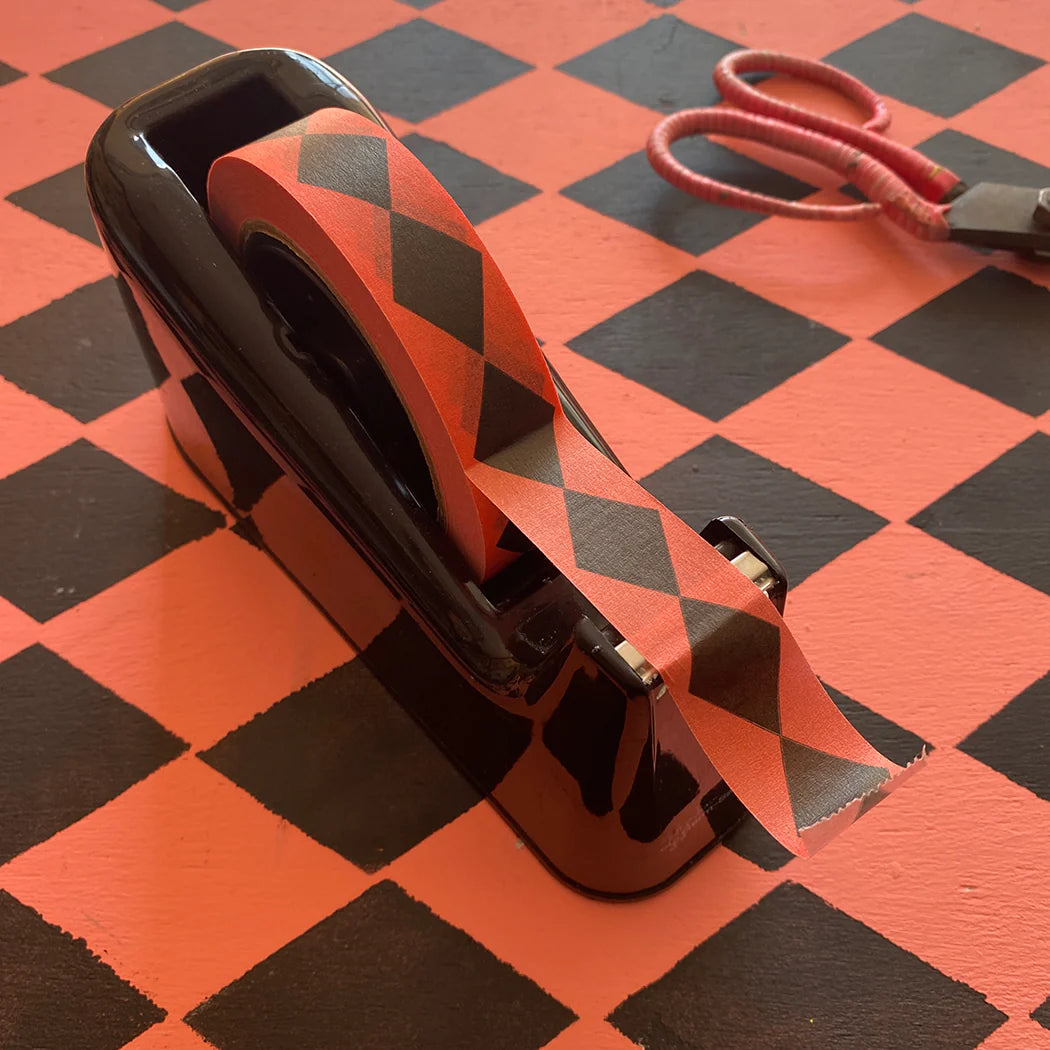 Black dispenser holding coral washi tape with a black diamond pattern.