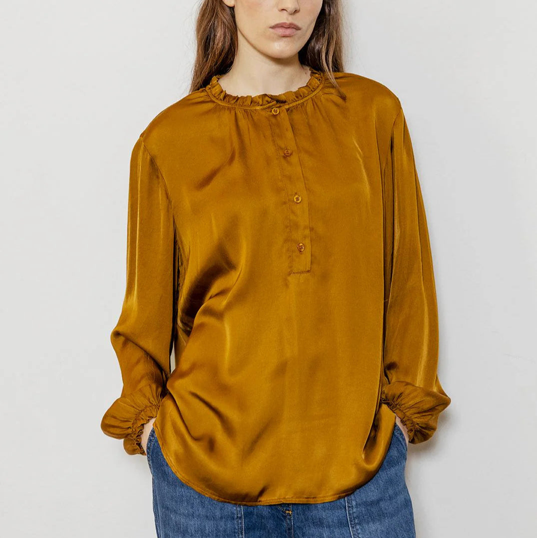 Woman wearing a mustard yellow blouse and blue jeans against a white background