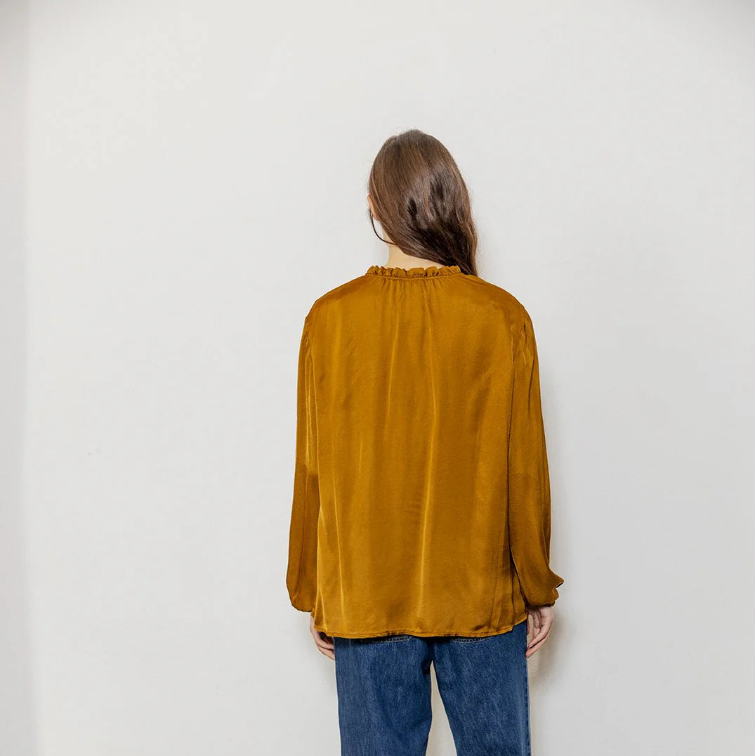 Person wearing a mustard yellow blouse and blue jeans against a white background