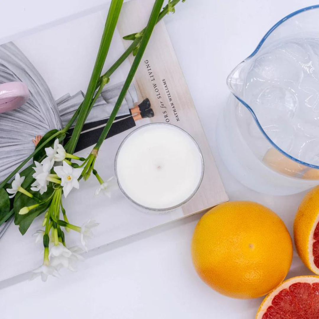 White scented candle in a clear glass jar, resting on a book.