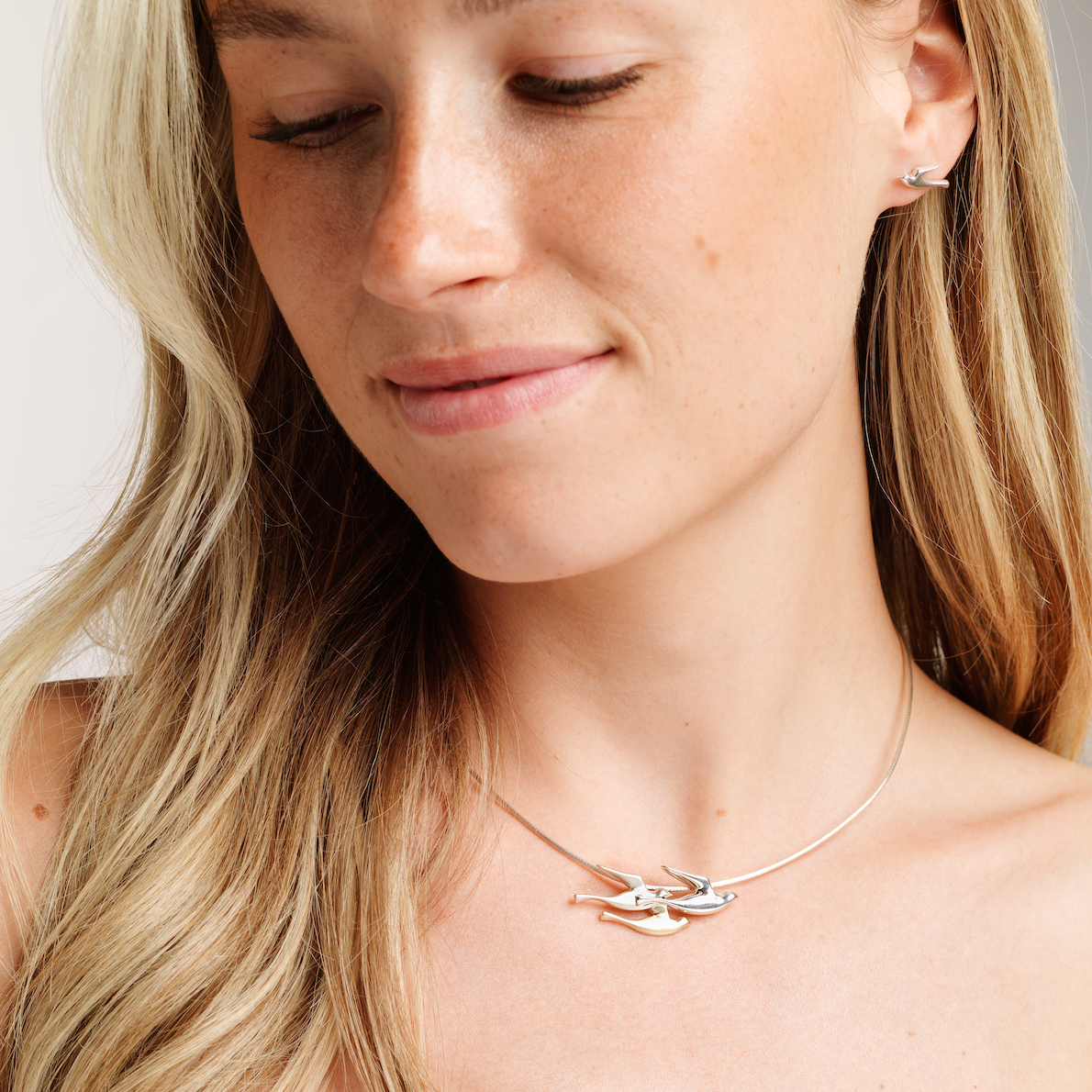 A woman wearing a stud birdland earring with matching necklace 