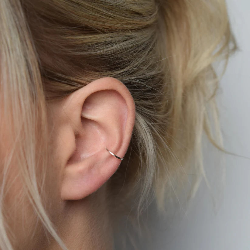 Silver ear cuff on a person's ear.  The cuff is a thin, simple hoop.