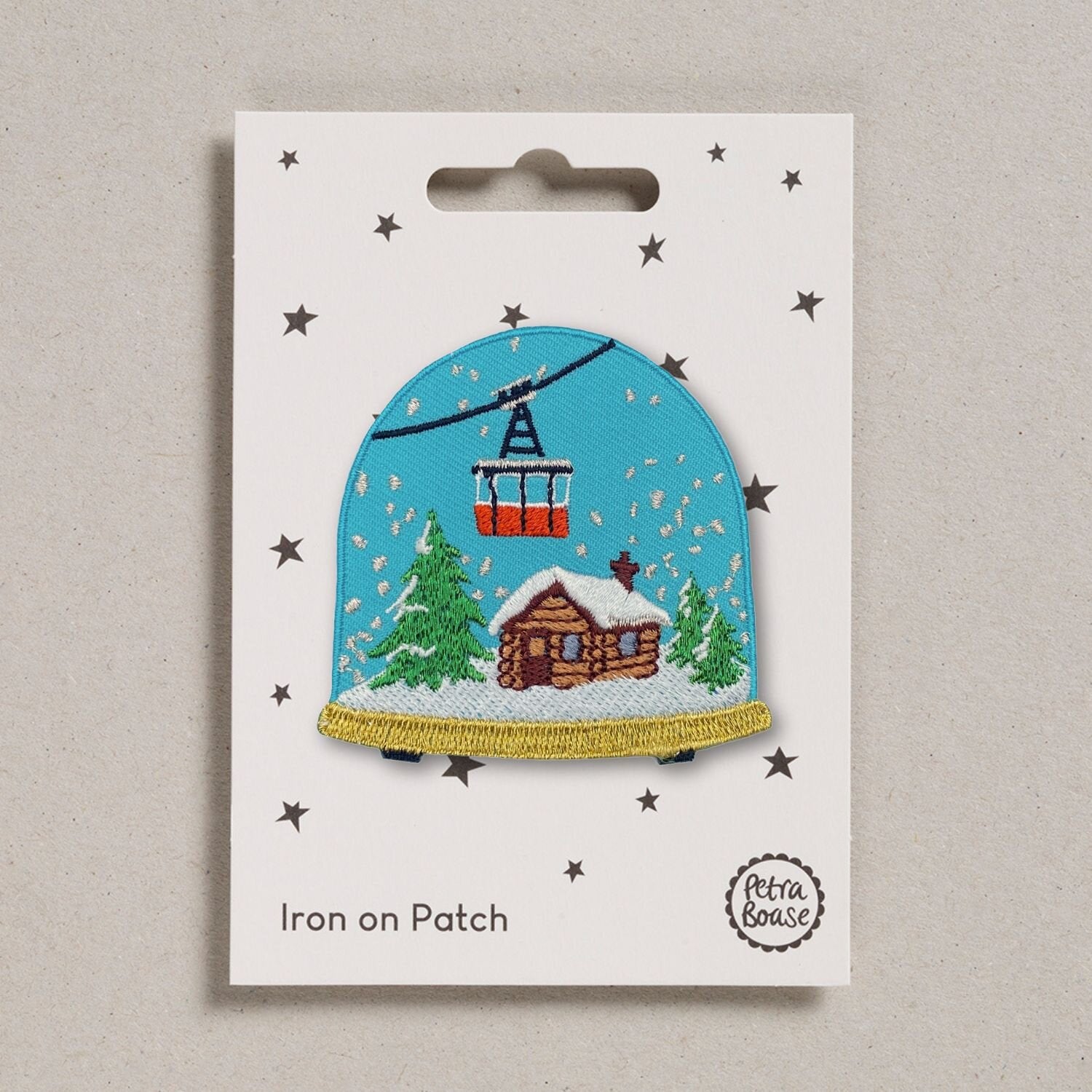 Embroidered iron-on patch depicting a snow globe scene: a cabin, snowy trees, and a cable car against a teal background.