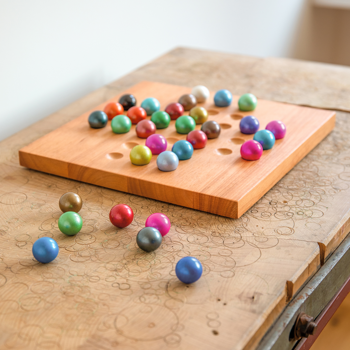A wooden board game with colorful round game pieces arranged on a carved wooden table, with a few pieces scattered nearby.