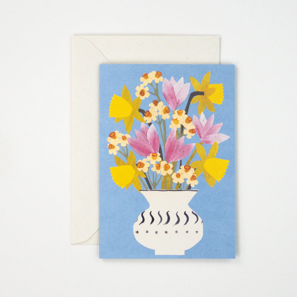 Greeting card featuring a stylized illustration of yellow daffodils and pink tulips in a white vase with black detailing, on