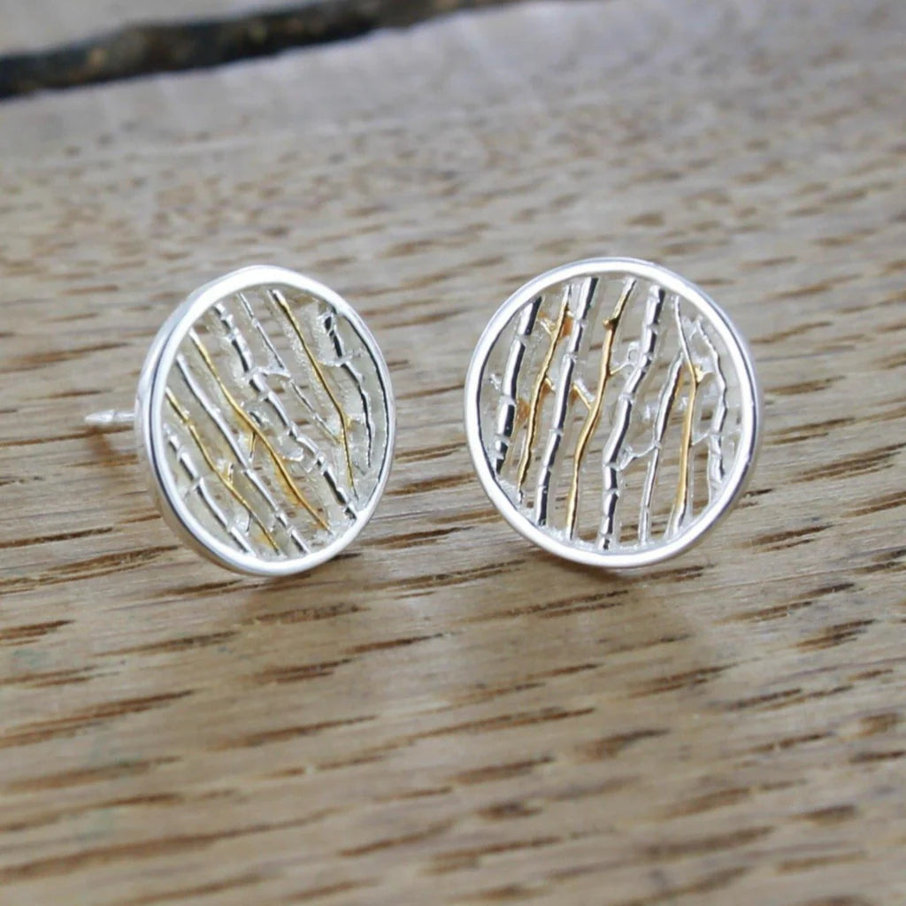 Pair of silver circular stud earrings with gold detailing; textured, linear design.