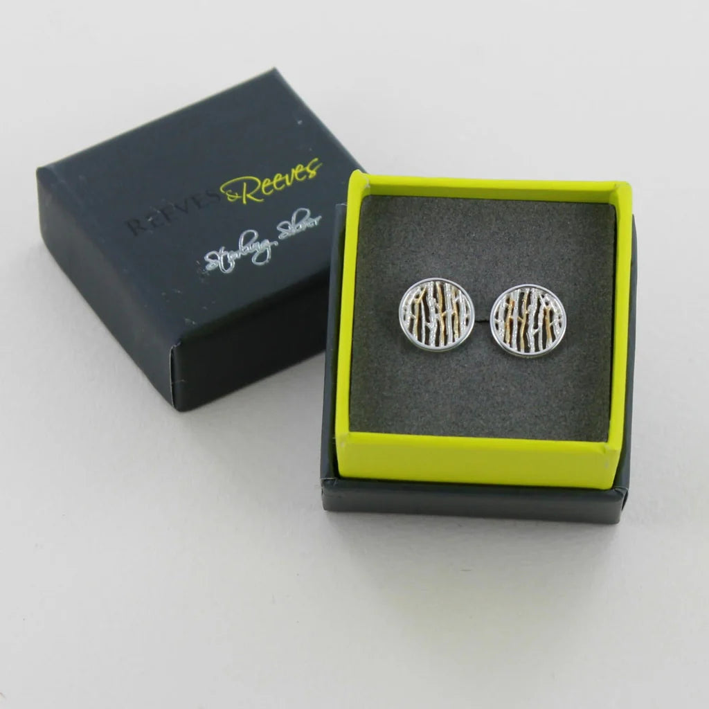 Pair of round sterling silver stud earrings with gold linear pattern.