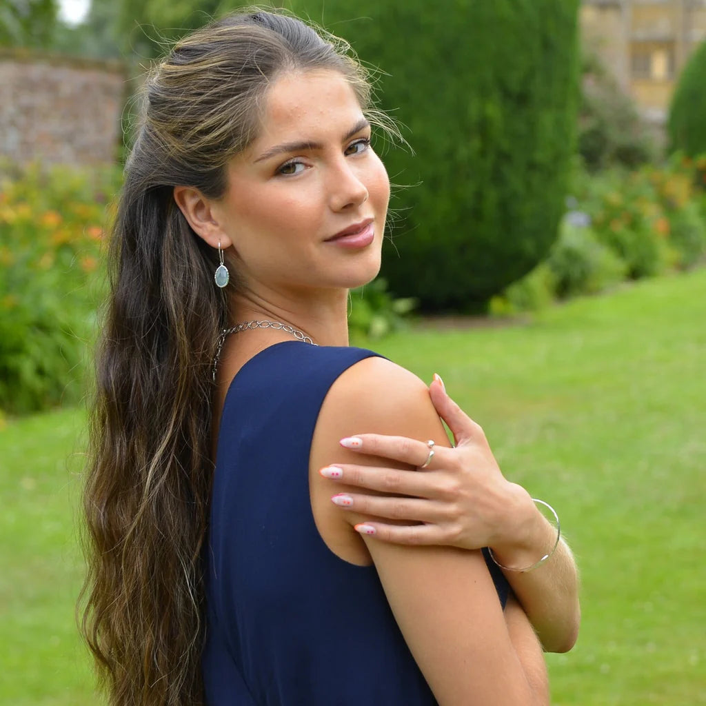 Woman with long brown hair wearing a navy sleeveless dress and oval-shaped earrings.