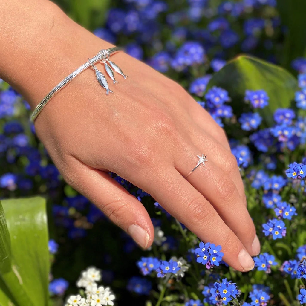 Silver bangle bracelet with three small fish charms and a delicate silver starfish ring.