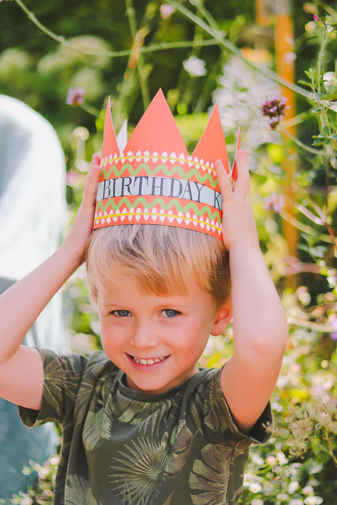 A young boy wearing an orange paper crown that says "Birthday King" on it.