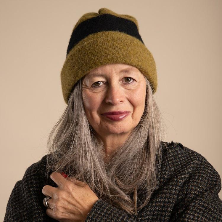 Woman with long gray hair wearing a mustard-colored knit beanie with a black stripe.