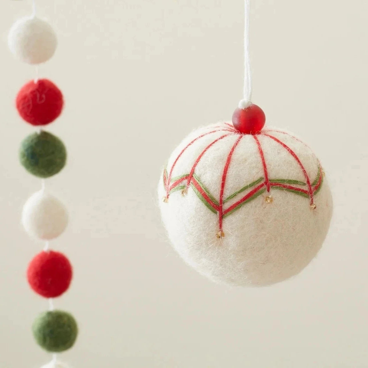 Off-white felt Christmas ornament with red and green embroidered details and small gold beads.
