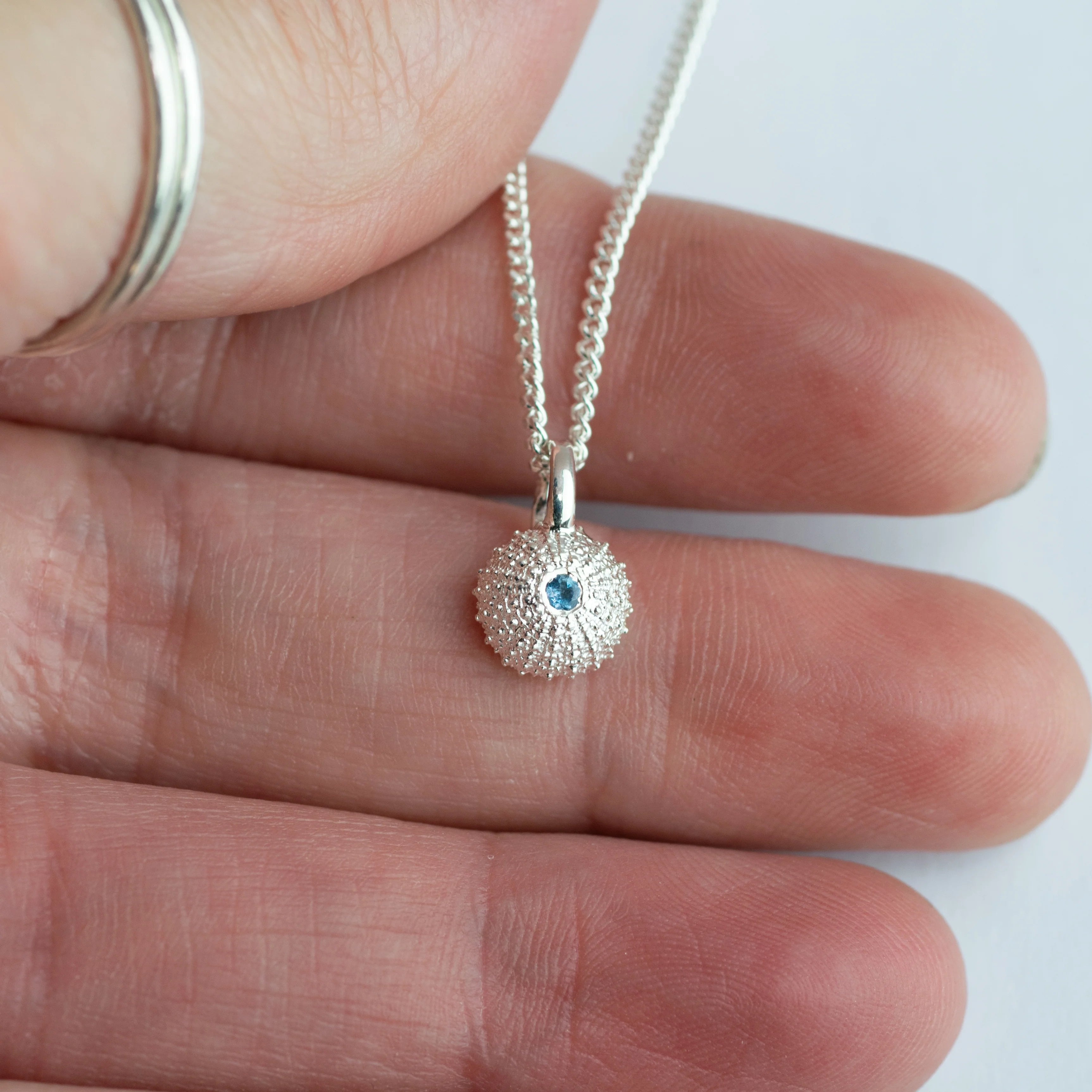 Silver necklace with a textured pendant held between fingers on a white background