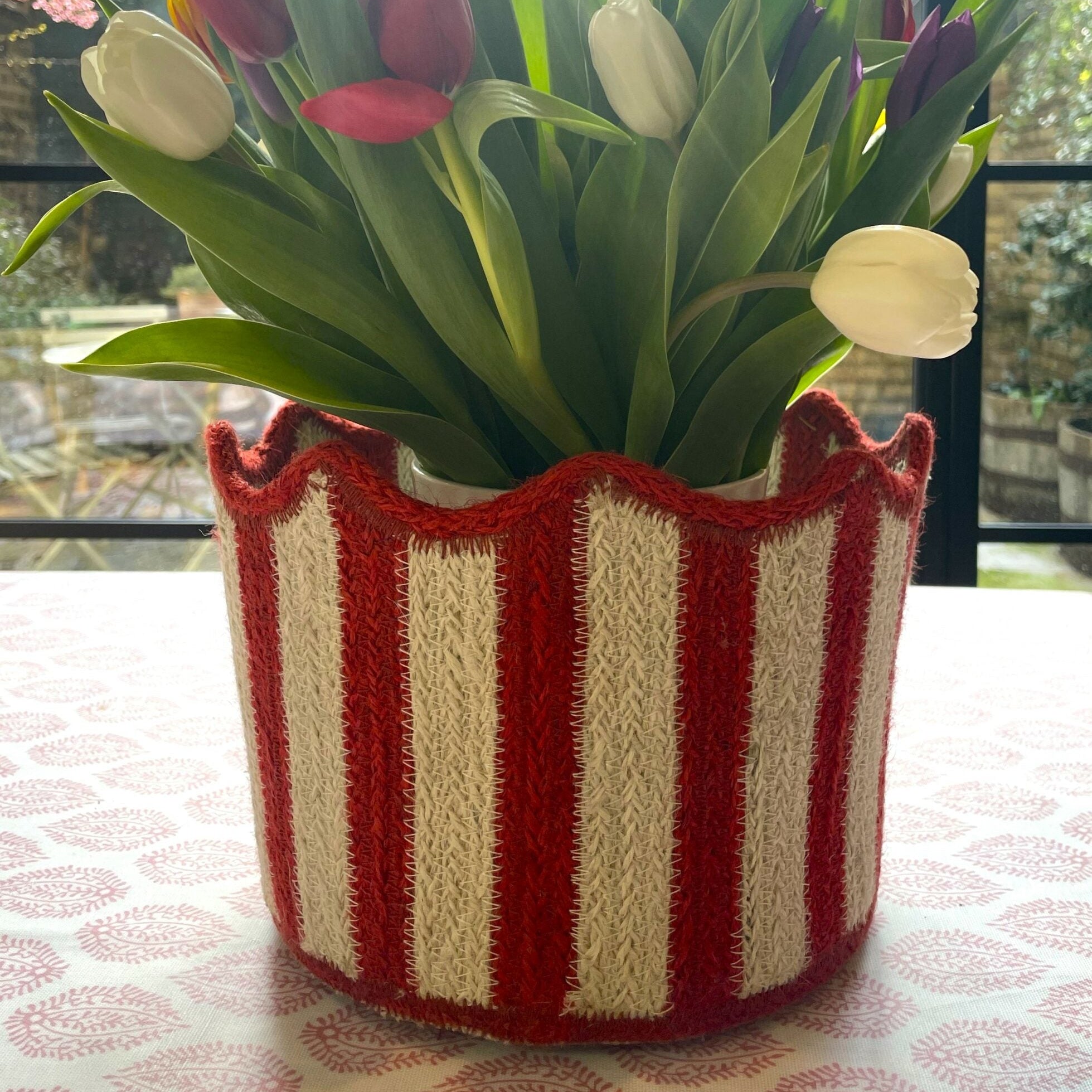 Bouquet of tulips in a red and white striped container on a table.