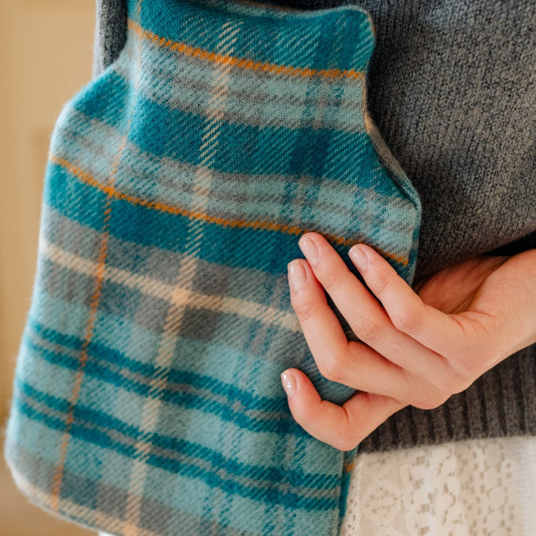 Person holding a blue plaid hot water bottle against a neutral background