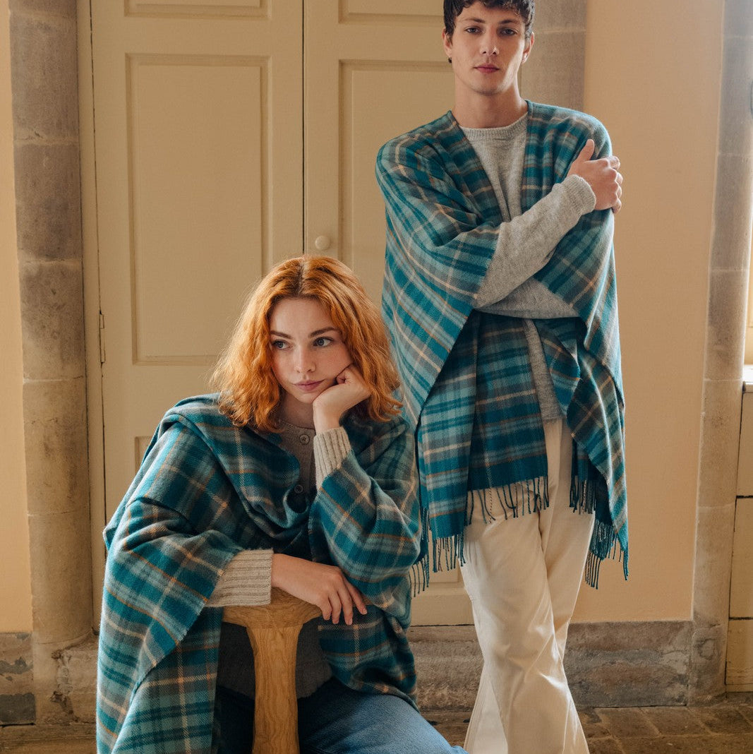 Two people wearing blue plaid shawls in a room with stone walls and wooden floors.