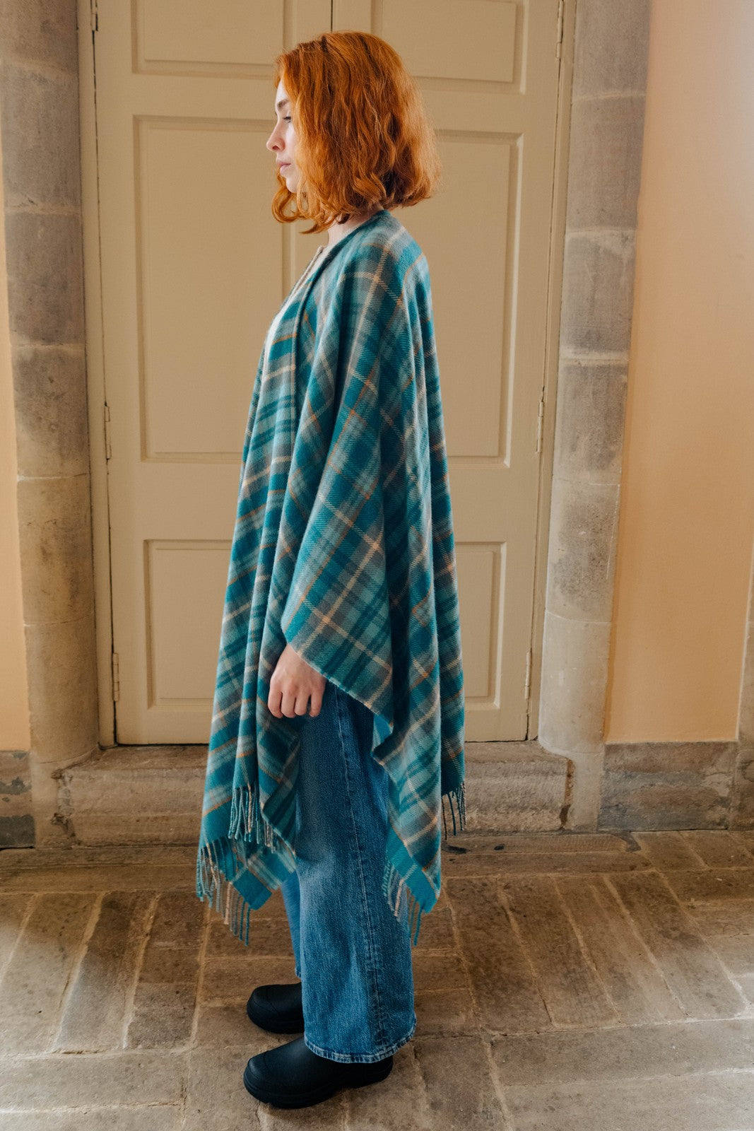 Woman wearing a blue plaid shawl standing in front of a stone wall.