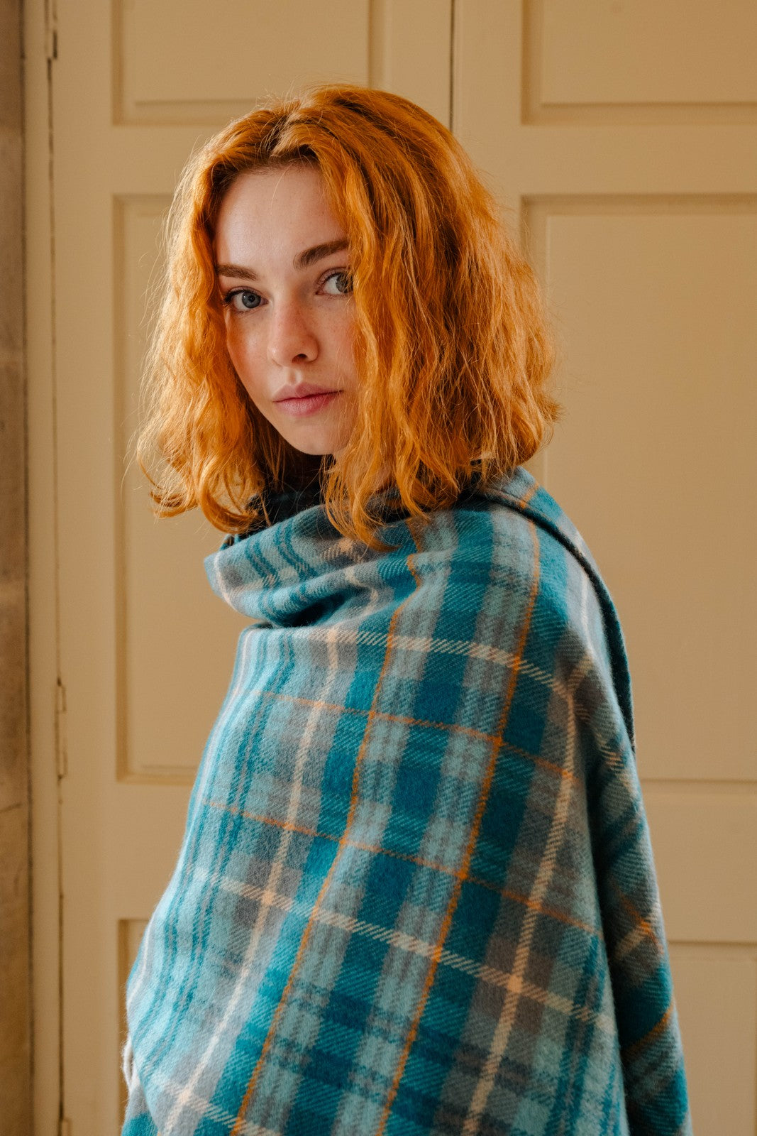 Woman wearing a blue plaid shawl against a beige wall