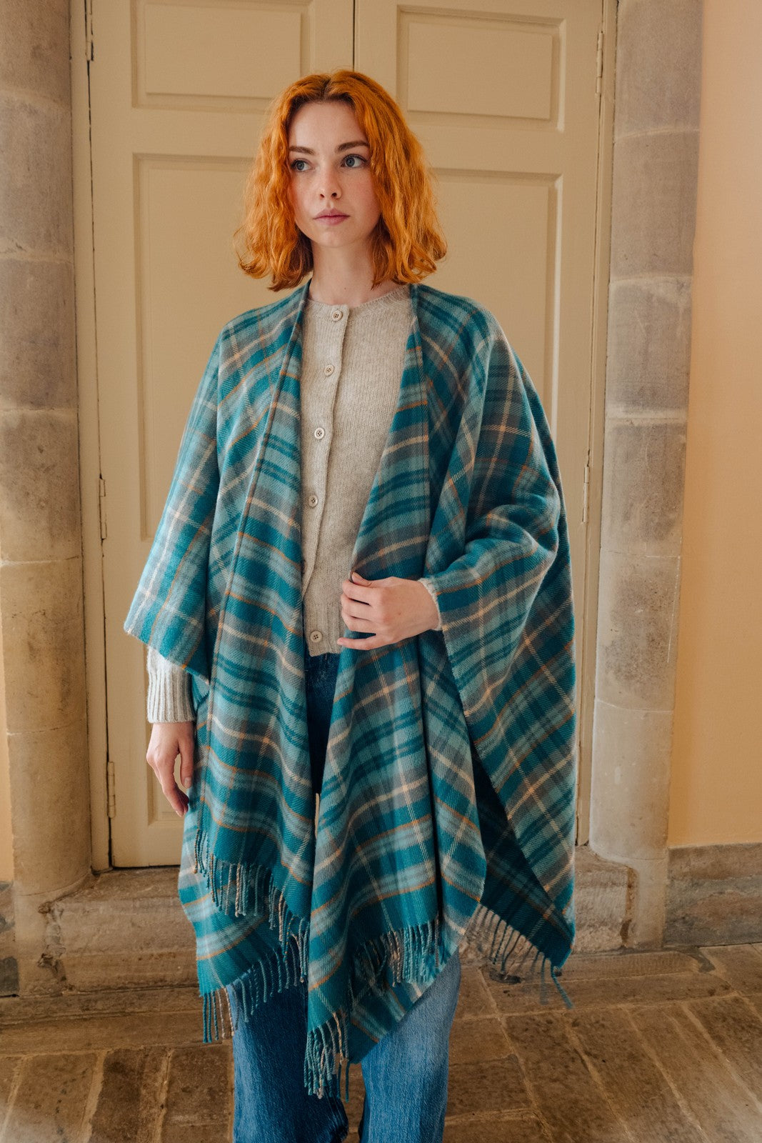 Woman wearing a blue plaid shawl standing in front of a stone wall.