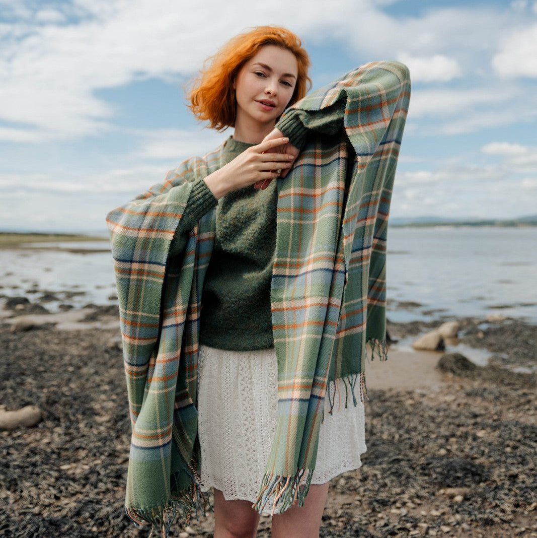 Woman with a plaid shawl standing on a beach with a blue sky and clouds in the background