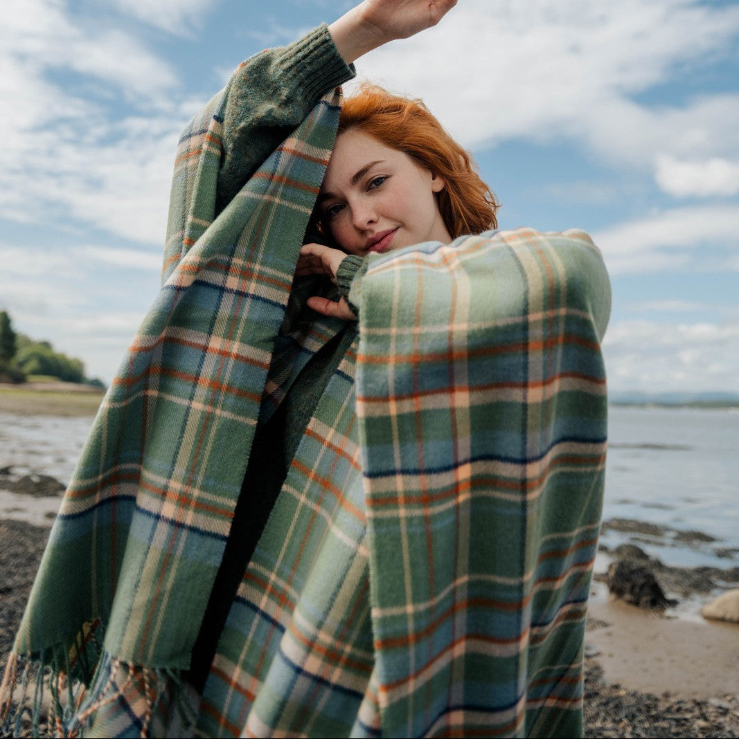 Person wrapped in a plaid blanket on a beach with a blue sky and clouds.