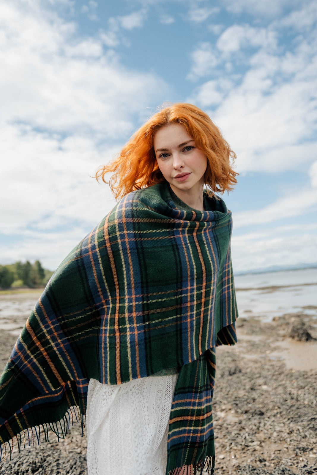 Woman with red hair wearing a green plaid shawl on a beach