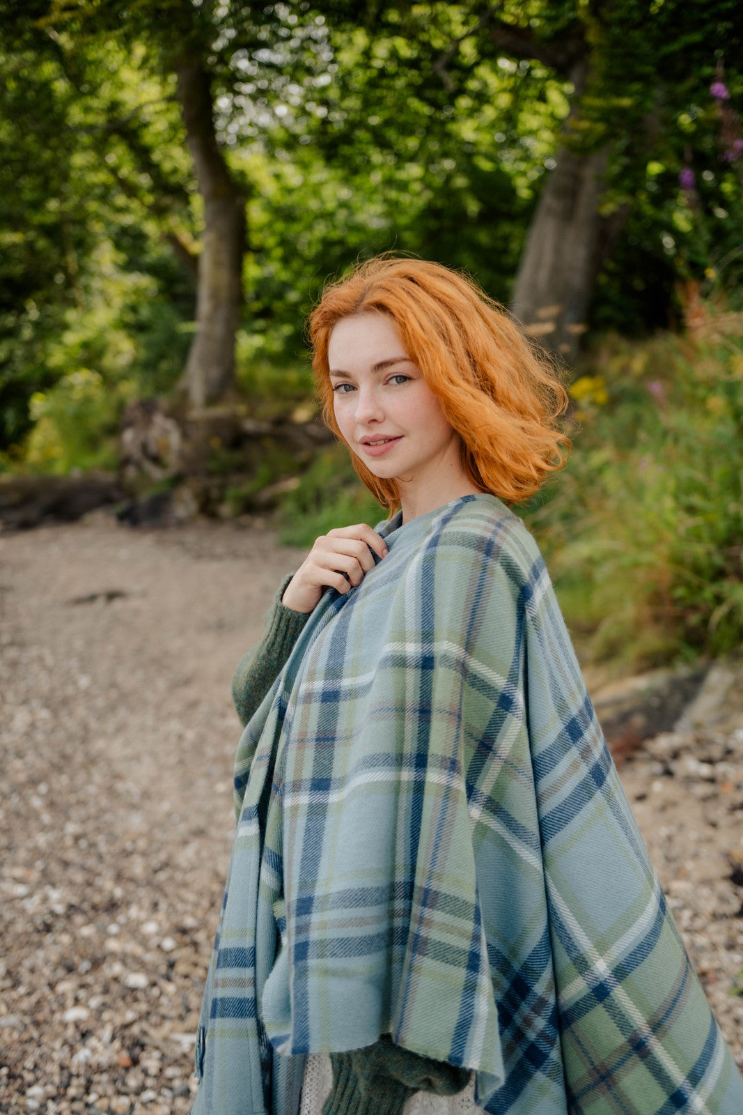 Woman with red hair wearing a blue plaid shawl in a natural setting