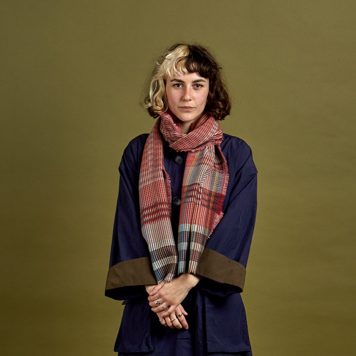 Person wearing a long dark coat and plaid scarf against a green background