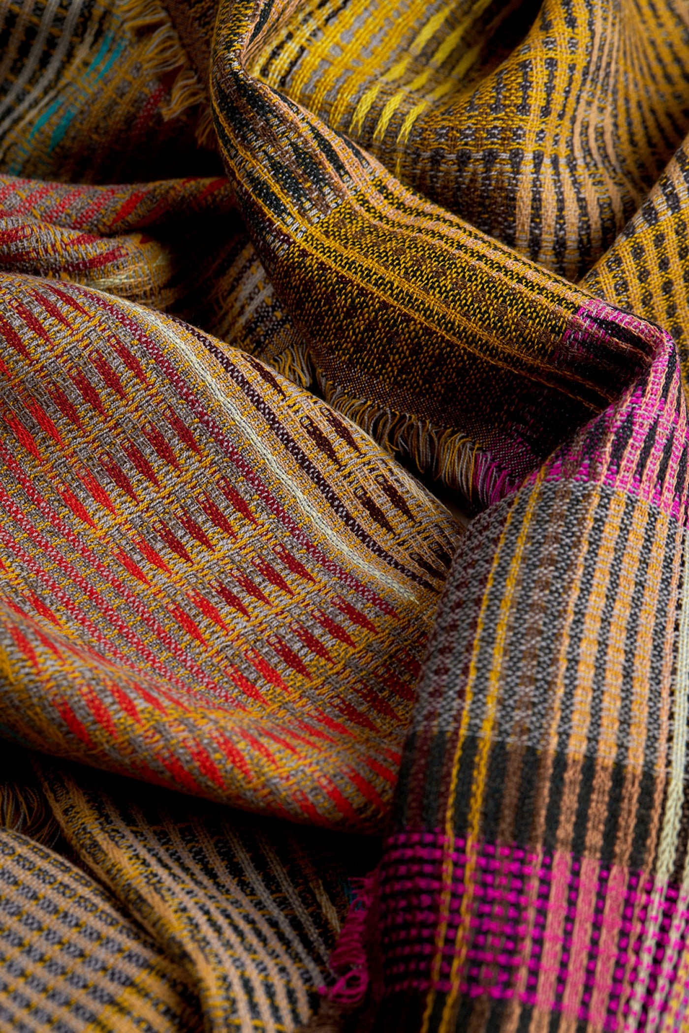 A close-up of a woven plaid scarf with a multicolor pattern featuring yellow, brown, red, gray, and bright pink stripes.