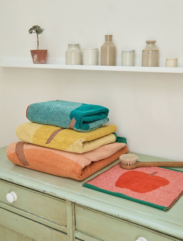 Stack of colorful towels on a green cabinet with a shelf in the background