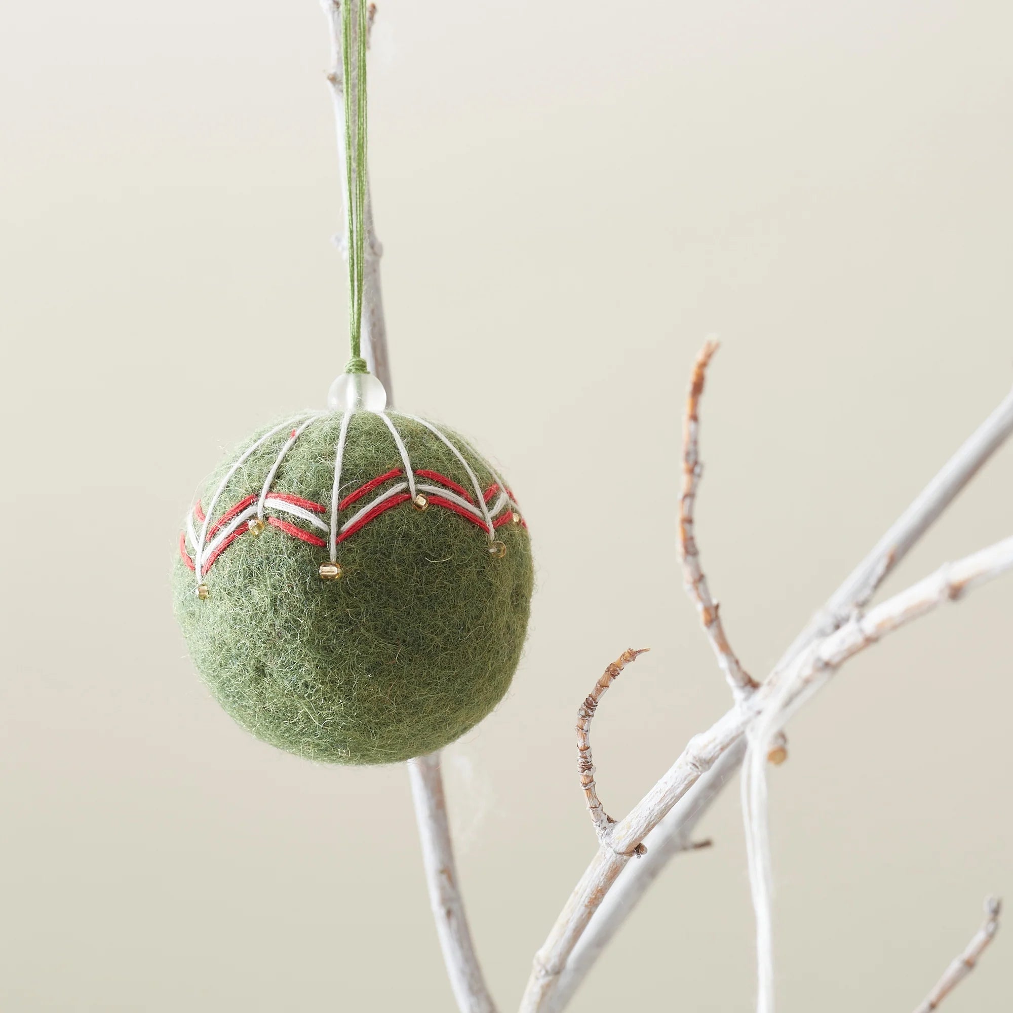 Green felt Christmas ornament with red and white embroidered details and small gold beads.