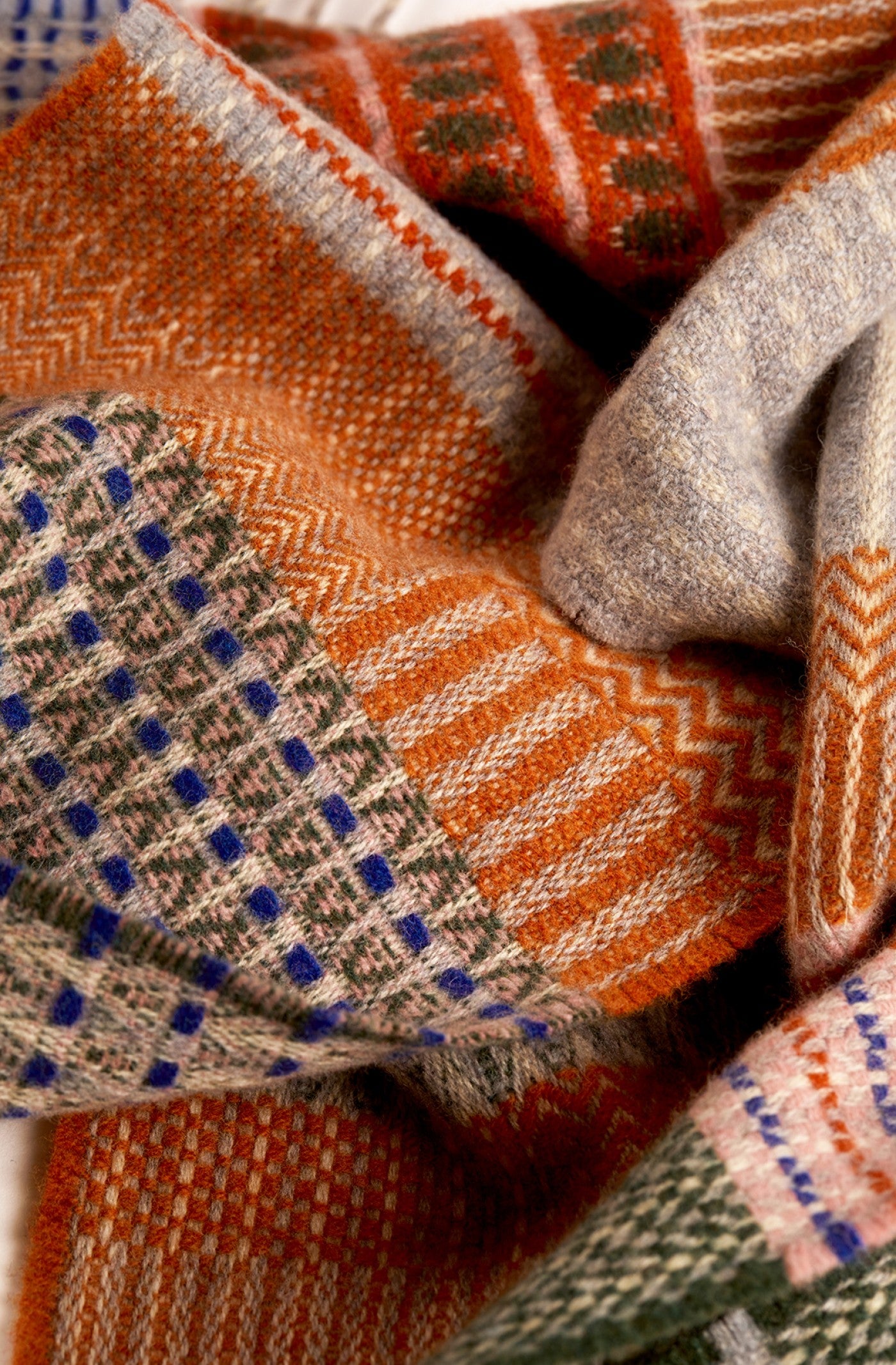 A close-up of a folded woven scarf or shawl with a multicolor patchwork pattern, featuring orange, gray, beige, blue, and green sections.