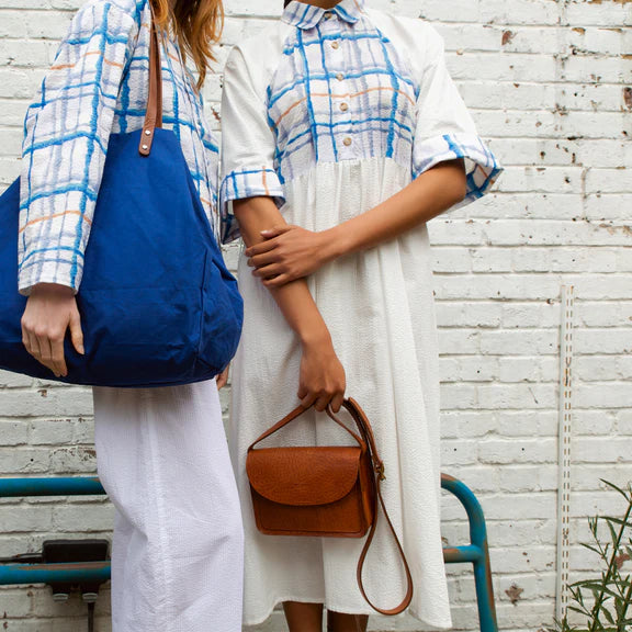 Two women model a blue tote bag and a brown leather shoulder bag.