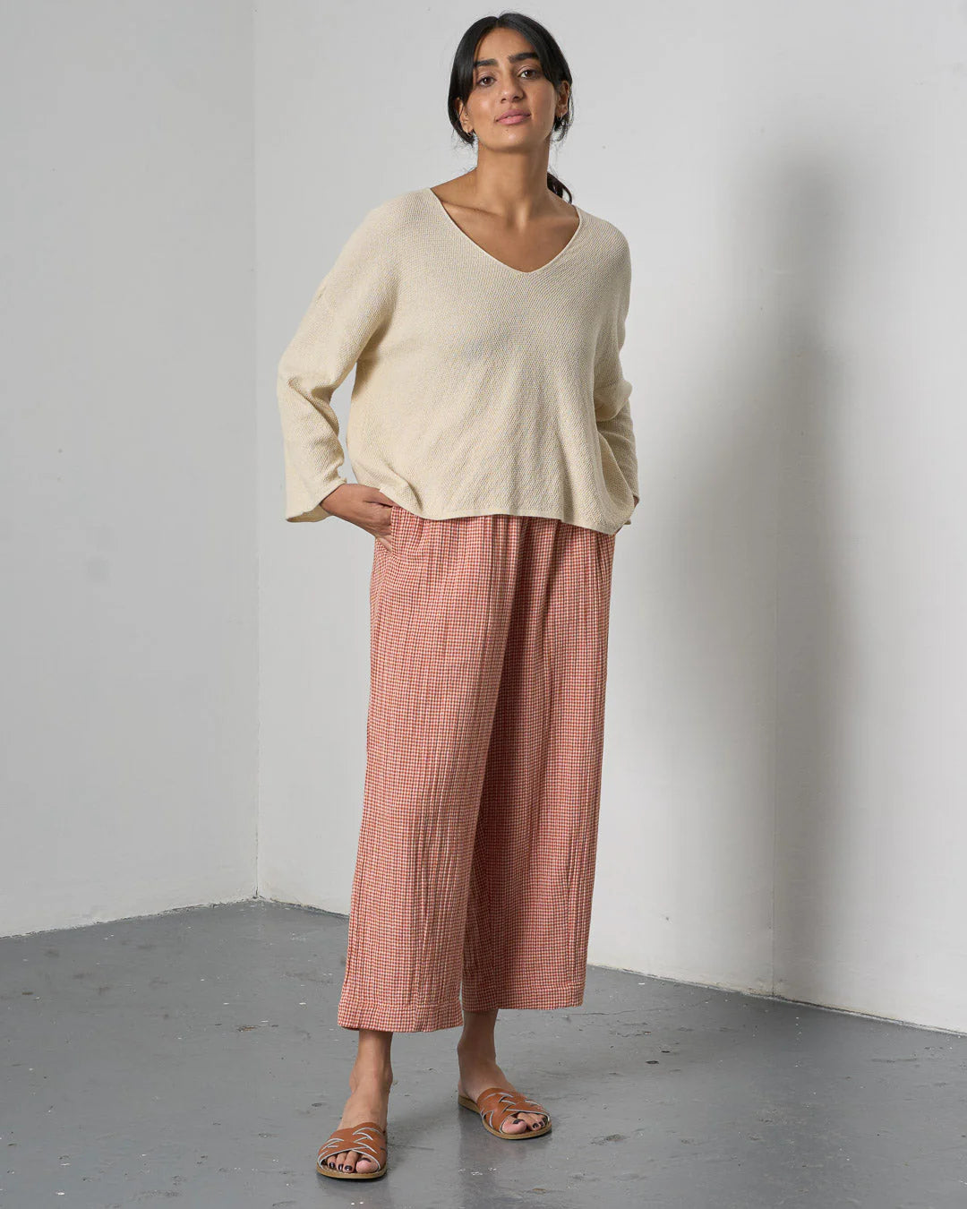 Woman wearing a beige sweater and pink checkered pants against a plain background